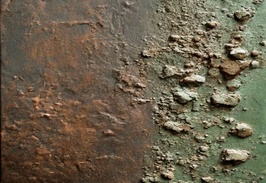 Bronze surface showing smooth dark patina beside bright powdery green corrosion
