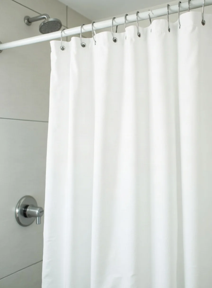 A clean white shower curtain and liner in a bright bathroom