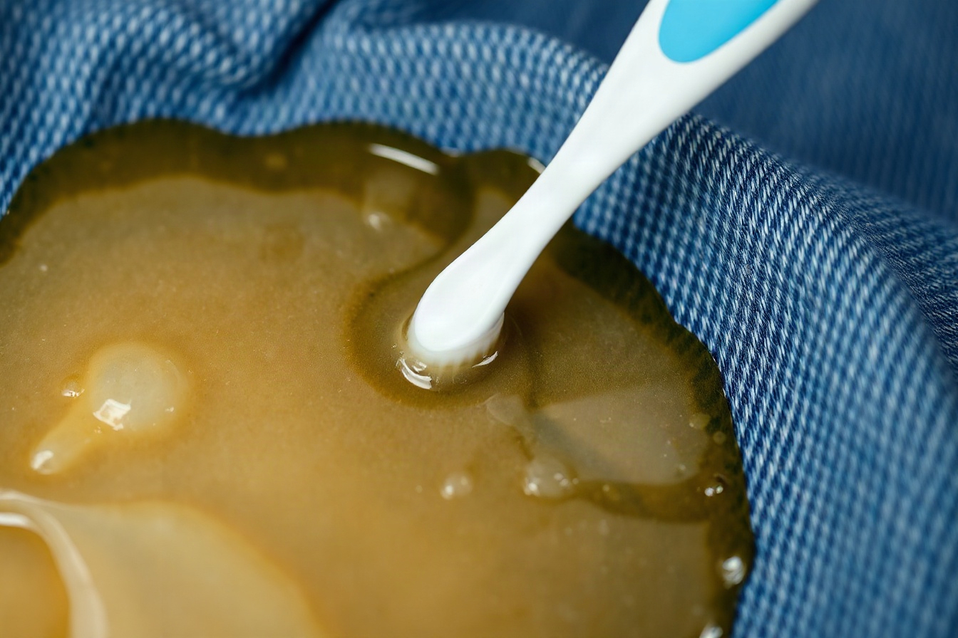 A toothbrush massaging liquid soap into an oil stain on denim fabric